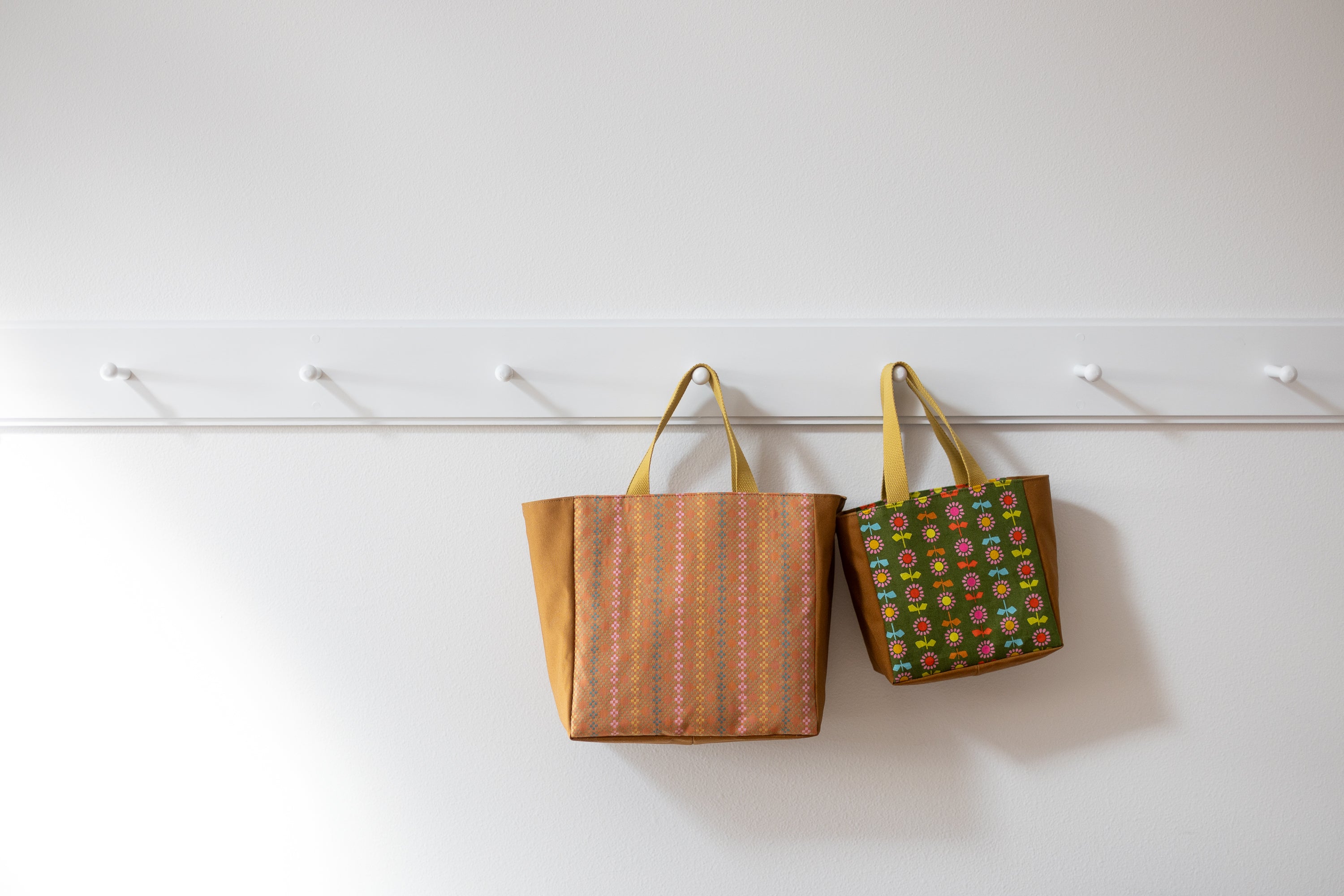 Two Fieldstone bags hanging on a rack against a white wall.